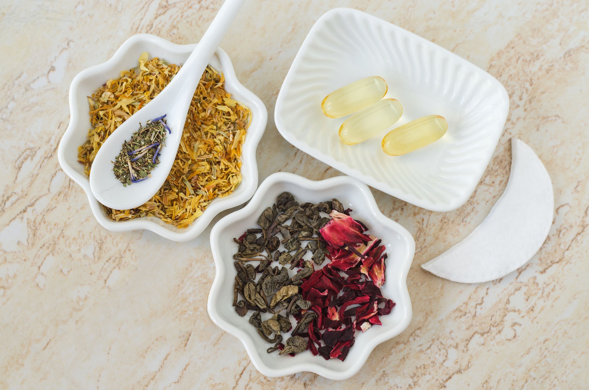 Small bowls with dry green tea leaves, marigold, hibiscus flowers and beauty vitamins. Natural skin care and healthy lifestyle concept. Homemade spa, beauty treatment recipe.